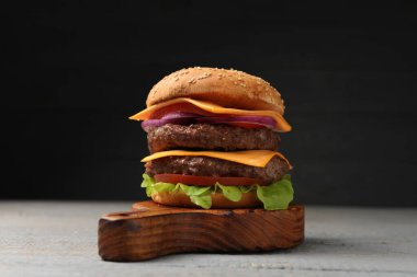 Etli, peynirli, sebzeli ve marullu leziz hamburger. Gri ahşap masa, yakın plan.