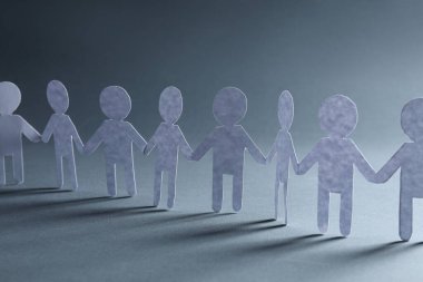 Takım çalışması konsepti. Gri arka planda el ele tutuşan insanların kağıt figürleri, yakın plan.