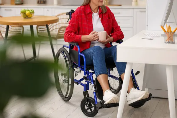 stock image Woman in wheelchair with cup of drink using computer at home, closeup