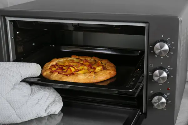 Woman taking baking pan with delicious pie from electric oven in kitchen, closeup