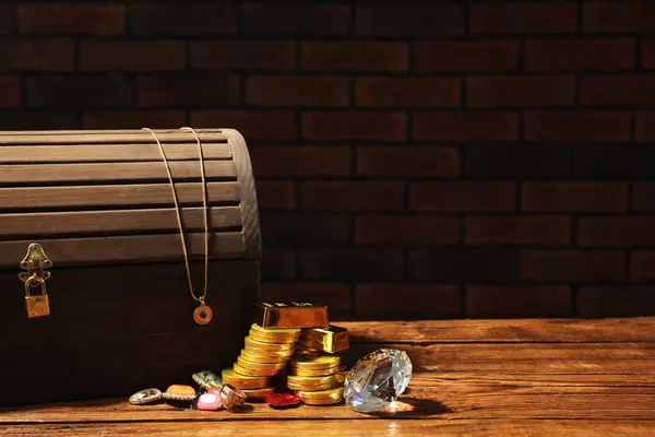 Treasure chest, gold bars, coins, jewelry and gemstones on wooden table. Space for text