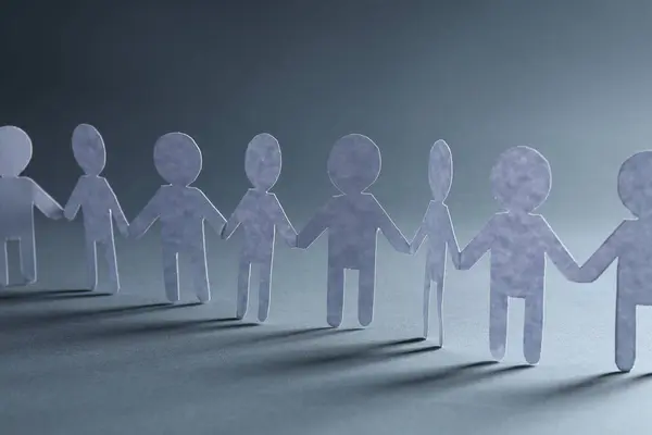 Teamwork concept. Paper figures of people holding hands on grey background, closeup