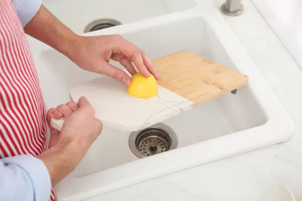 Man rubbing cutting board with lemon at sink in kitchen, closeup