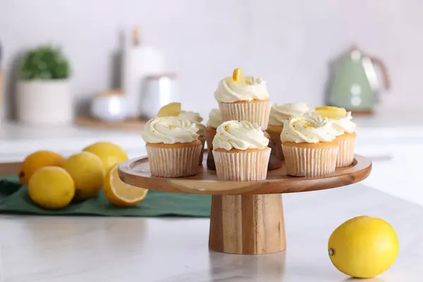 Delicious lemon cupcakes with white cream and lemons on table indoors