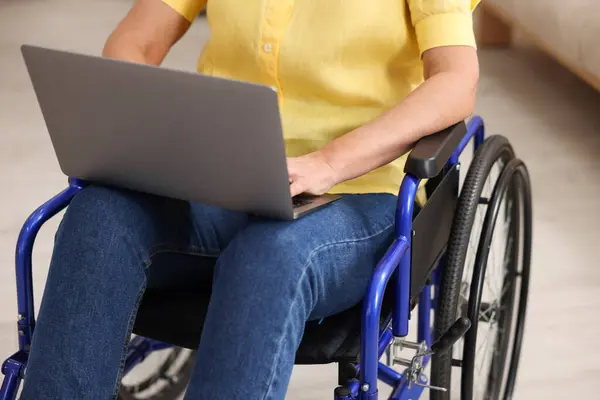 Woman in wheelchair using laptop indoors, closeup