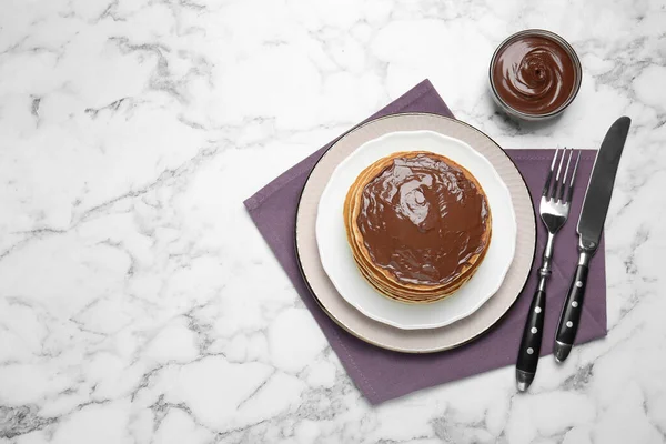 Tasty pancakes with chocolate paste and cutlery on white marble table, flat lay. Space for text