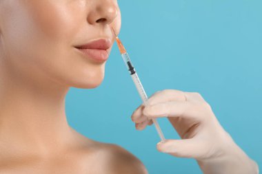 Doktor açık mavi arka planda genç bir kadına yüz enjeksiyonu yapıyor, yakın plan. Estetik ameliyat