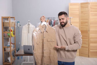 Kuru temizleme servisi. Kapalı mekanda naylon torba içinde ceketli duygusal bir adam.