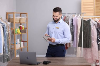 Kuru temizleme servisi. Mutlu işçi iş yerinde notlar alıyor.