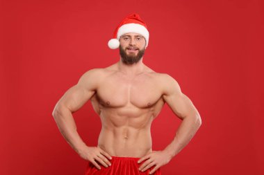 Kırmızı arka planda Noel Baba şapkalı kaslı genç adam.