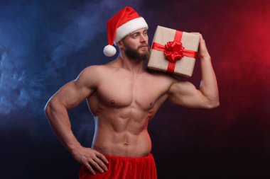 Kaslı vücutlu çekici bir genç. Elinde renkli bir Noel hediyesi kutusu var.