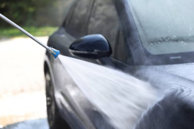 Washing auto with high pressure water jet at outdoor car wash, closeup