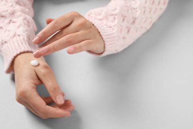 Woman applying cosmetic cream onto hand on light grey background, closeup. Space for text