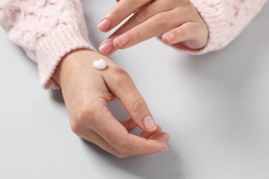 Woman applying cosmetic cream onto hand on light grey background, closeup