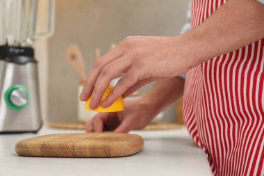 Adam mutfaktaki ışık masasında ahşap kesme tahtasına limon suyu sürüyor.