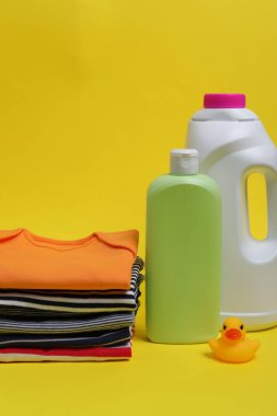 Çamaşır deterjanı, bebek kıyafetleri ve sarı arka planda plastik ördek.