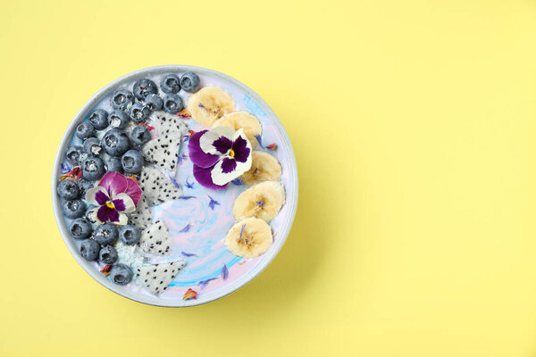 Delicious smoothie bowl with fresh fruits, blueberries and flowers on yellow background, top view. Space for text