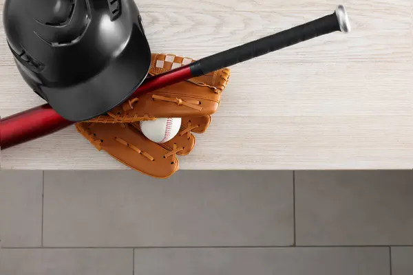 Baseball bat, batting helmet, leather glove and ball on wooden bench indoors, above view. Space for text