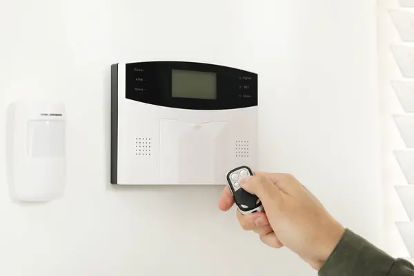Home security system. Man using alarm key fob indoors, closeup