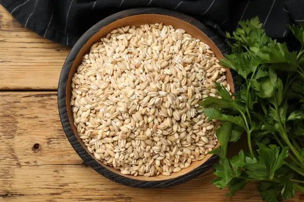 Stock image Dry pearl barley in bowl and parsley on wooden table, top view