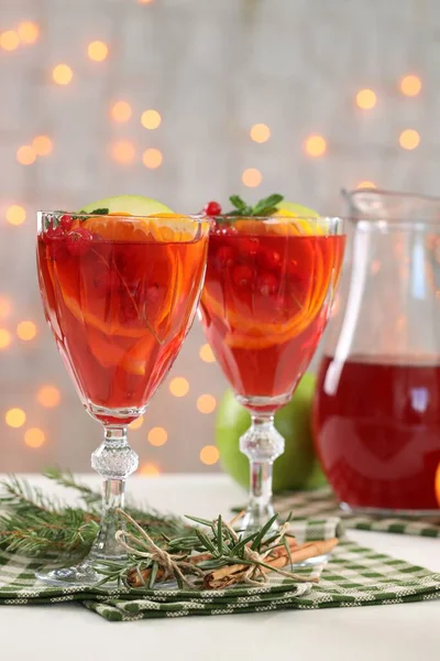 Christmas Sangria cocktail in glasses, cinnamon sticks and fir tree branch on white table against blurred lights