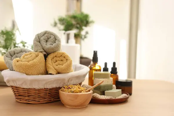 Dry flowers, soap bars, bottles of essential oils, jar with cream and towels on wooden table indoors, space for text. Spa time