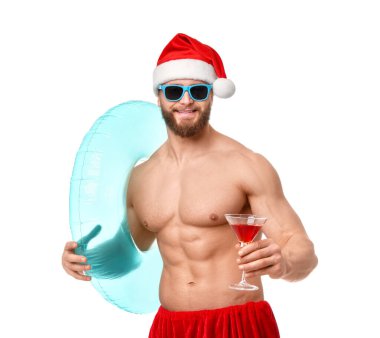Noel Baba şapkalı kaslı genç adam. Beyaz arka planda şişme yüzük ve kokteyl var.