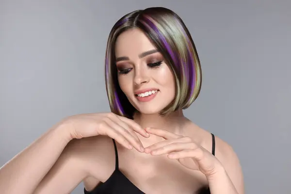 Hair styling. Attractive woman with colorful hair on grey background