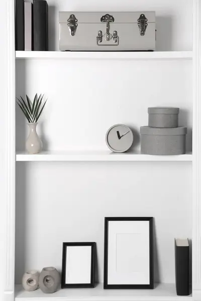White shelves with clock, photo frames and different decor indoors. Interior design