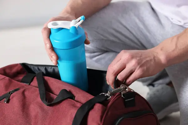 Young man putting shaker with protein into bag on blurred background, closeup