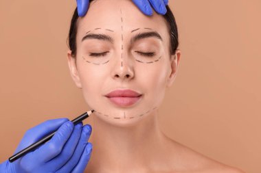 Bej arka planda estetik ameliyat için kadının yüzüne işaretler çizen doktor.