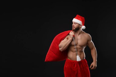 Siyah arka planda hediyeler taşıyan Noel Baba şapkalı kaslı genç adam, mesaj için yer var.