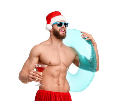 Noel Baba şapkalı kaslı genç adam. Beyaz arka planda şişme yüzük ve kokteyl var.