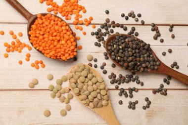 Açık ahşap masada farklı türde mercimeği olan kaşıklar.