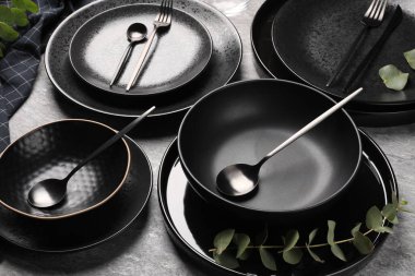 Masa dekorları çok şık. Gri yüzeyde tabaklar, çatal bıçak takımı ve okaliptüs dalı