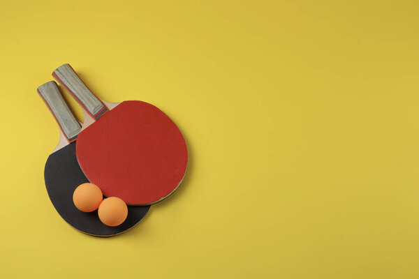 Ping pong balls and rackets on yellow background, flat lay. Space for text