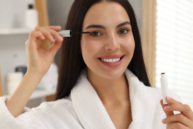 Güzel bir kadın banyoda kirpiklerine serum sürüyor. Kozmetik ürünü