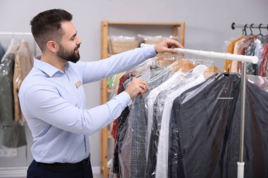 Kuru temizleme servisi. Mutlu işçi, içerideki askılardan kıyafet seçiyor.