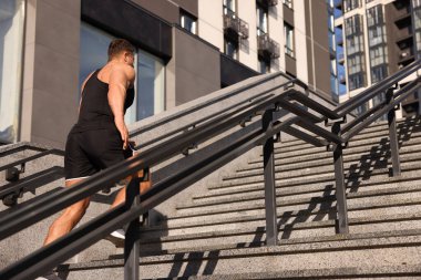 Güneşli bir günde merdivenlerden koşarak çıkan bir adam.