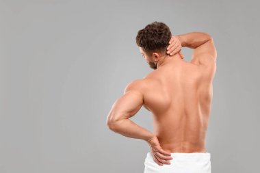 Man suffering from back and neck pain on grey background, back view. Space for text clipart