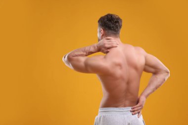 Man suffering from back and neck pain on orange background, back view. Space for text clipart