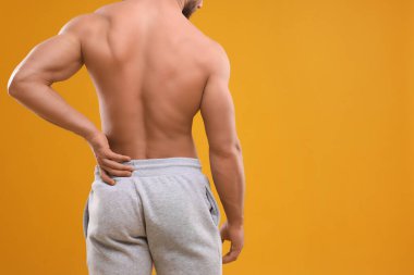 Man suffering from back pain on orange background, back view. Space for text clipart