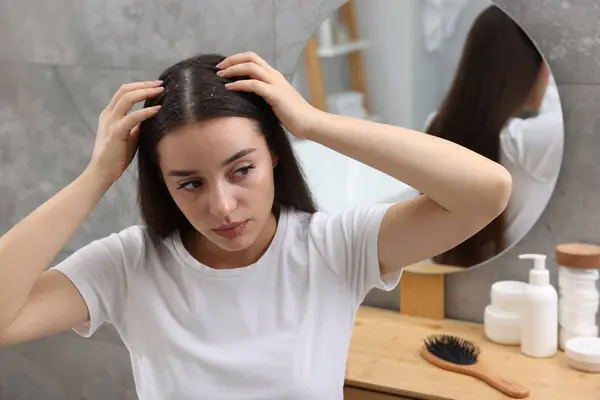 Woman examining her hair and scalp at home. Dandruff problem