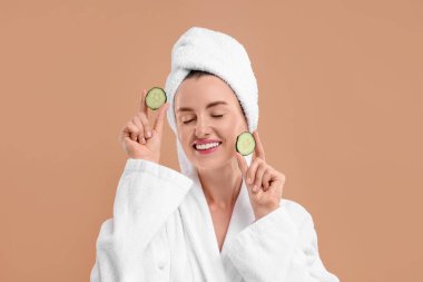 Bornozlu, bej arka planda salatalık parçaları olan güzel bir kadın.