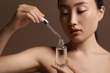 Kahverengi arka planda kozmetik serumu şişesi olan güzel genç bir kadın. Yakın plan.