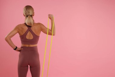 Pembe arka planda elastik direnç bandıyla egzersiz yapan bir kadın. Metin için boşluk