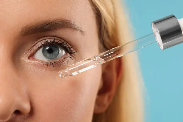 stock image Woman applying cosmetic serum onto her face on light blue background, closeup