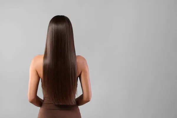 Hair styling. Woman with straight long hair on grey background, back view and space for text
