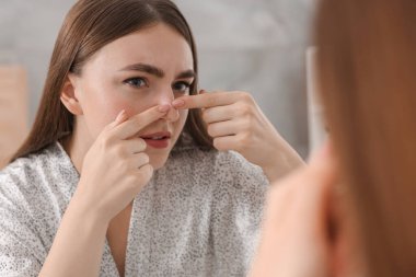 Cilt sorunu olan genç bir kadın aynaya bakıyor.