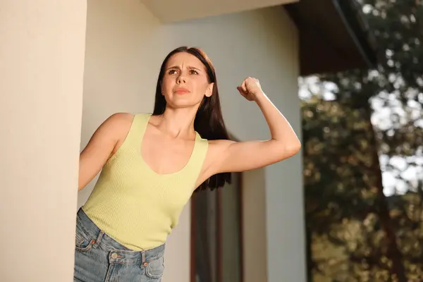 Angry woman showing fist near house, low angle view. Annoying neighbour